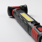 Gros plan du bandeau LED COB allumé et du bouton de commande d'une lampe de travail noire et rouge